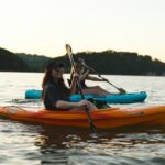 Woman in blue shirt and blue denim jeans riding orange kayak on water during daytime
