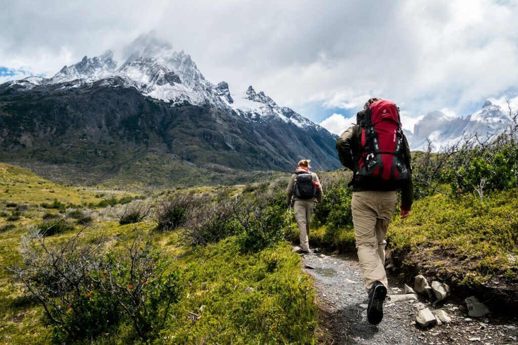 Two person walking towards mountain covered with snow